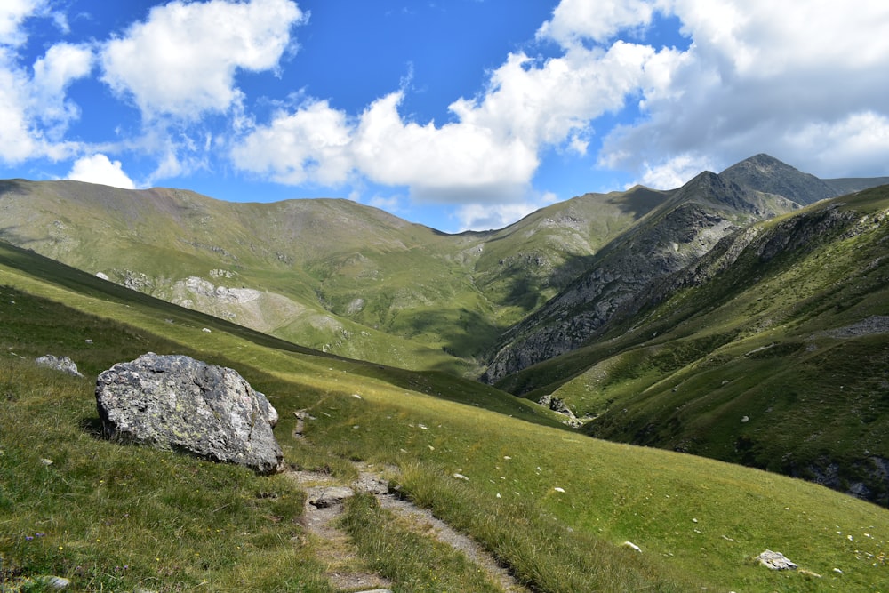 green grass field and mountains under blue sky and white clouds during daytime