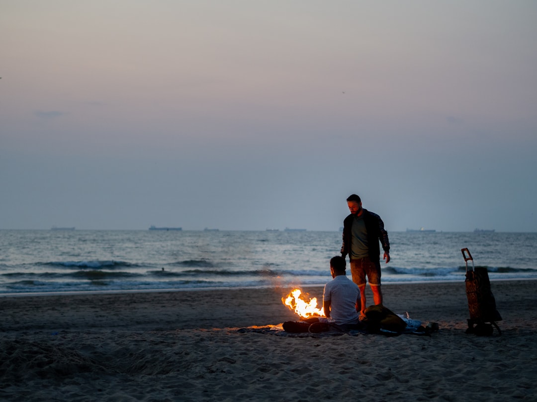 man and woman sitting on beach shore during sunset