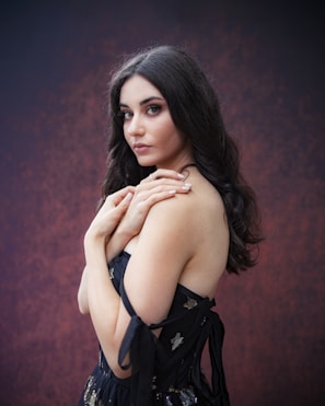 Portrait of a model with soft lighting, wearing a sleek black dress against a dark, minimal background.