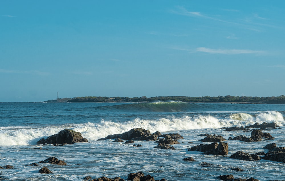 ocean waves crashing on rocks under blue sky during daytime