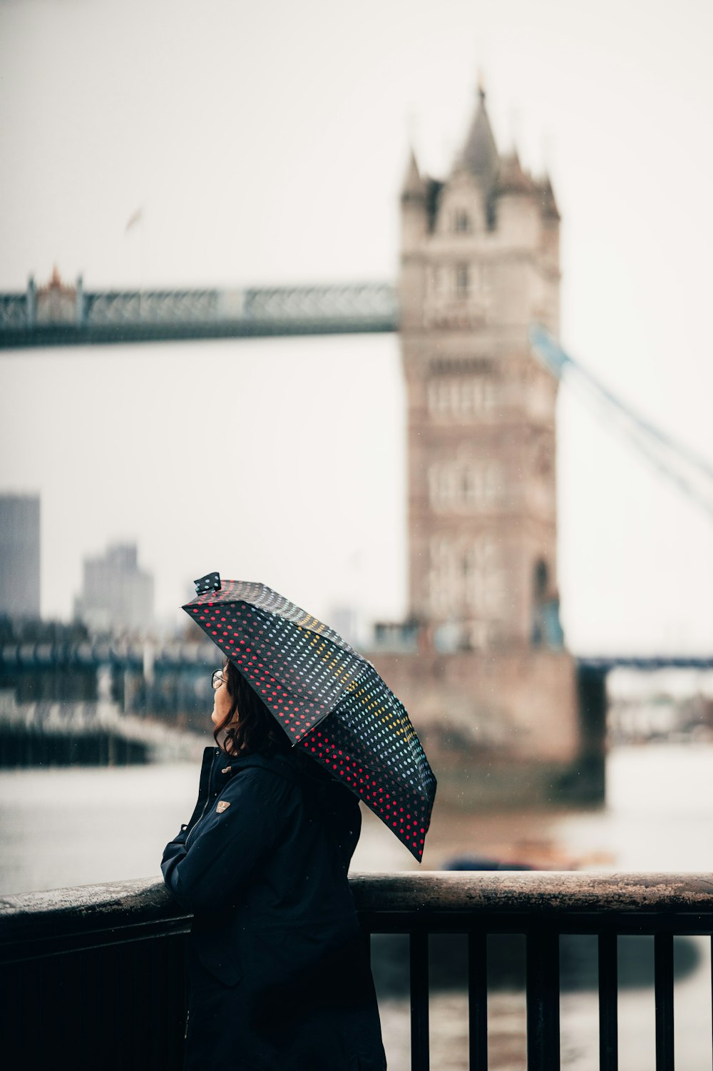 mulher na jaqueta preta que segura o guarda-chuva vermelho e branco