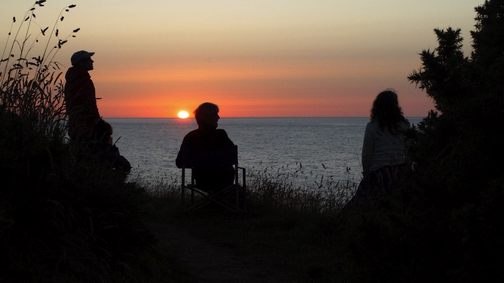 silhouette of man and woman sitting on chair near sea during sunset