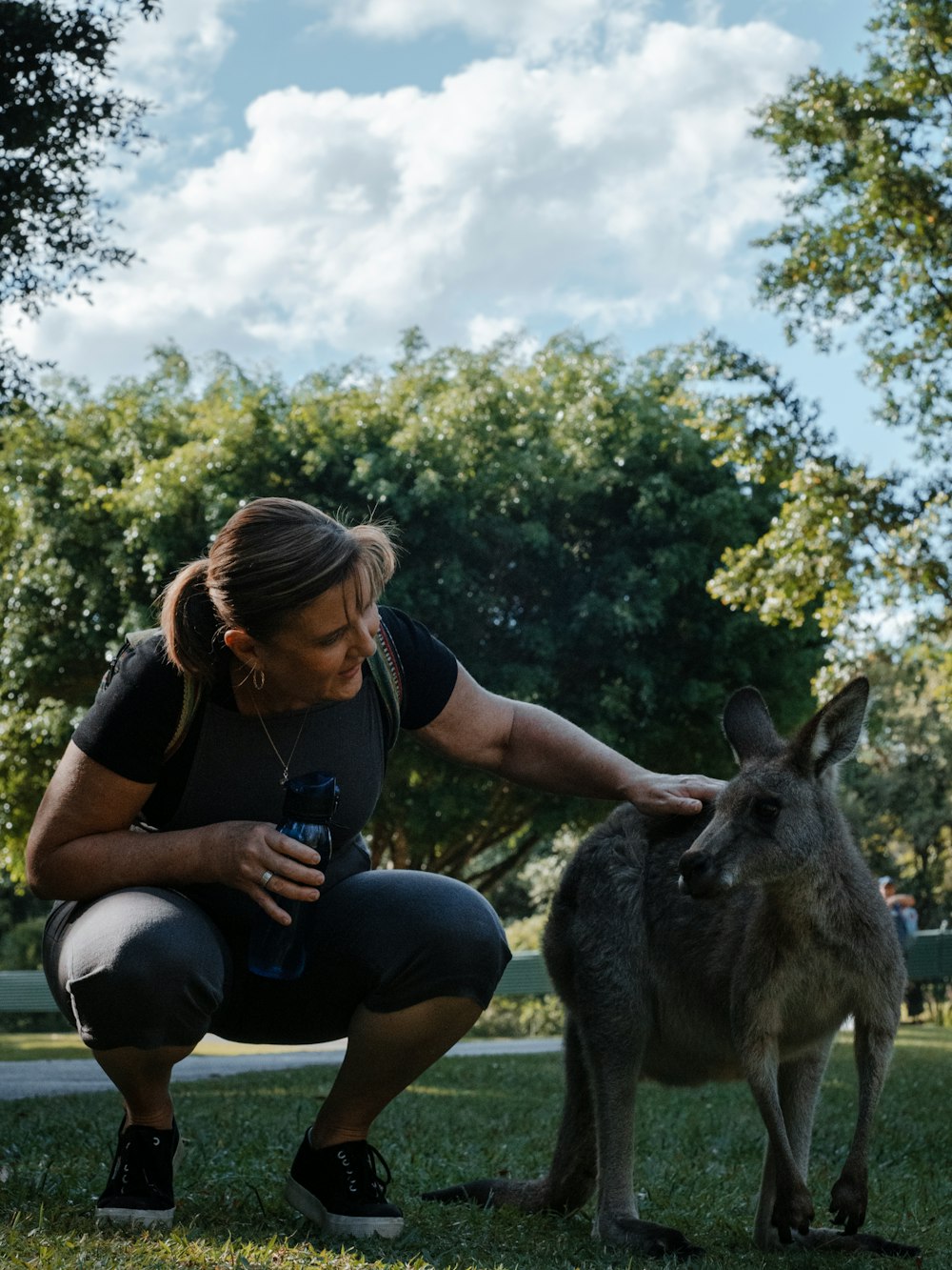 Frau im schwarzen T-Shirt sitzt tagsüber neben grauem Känguru