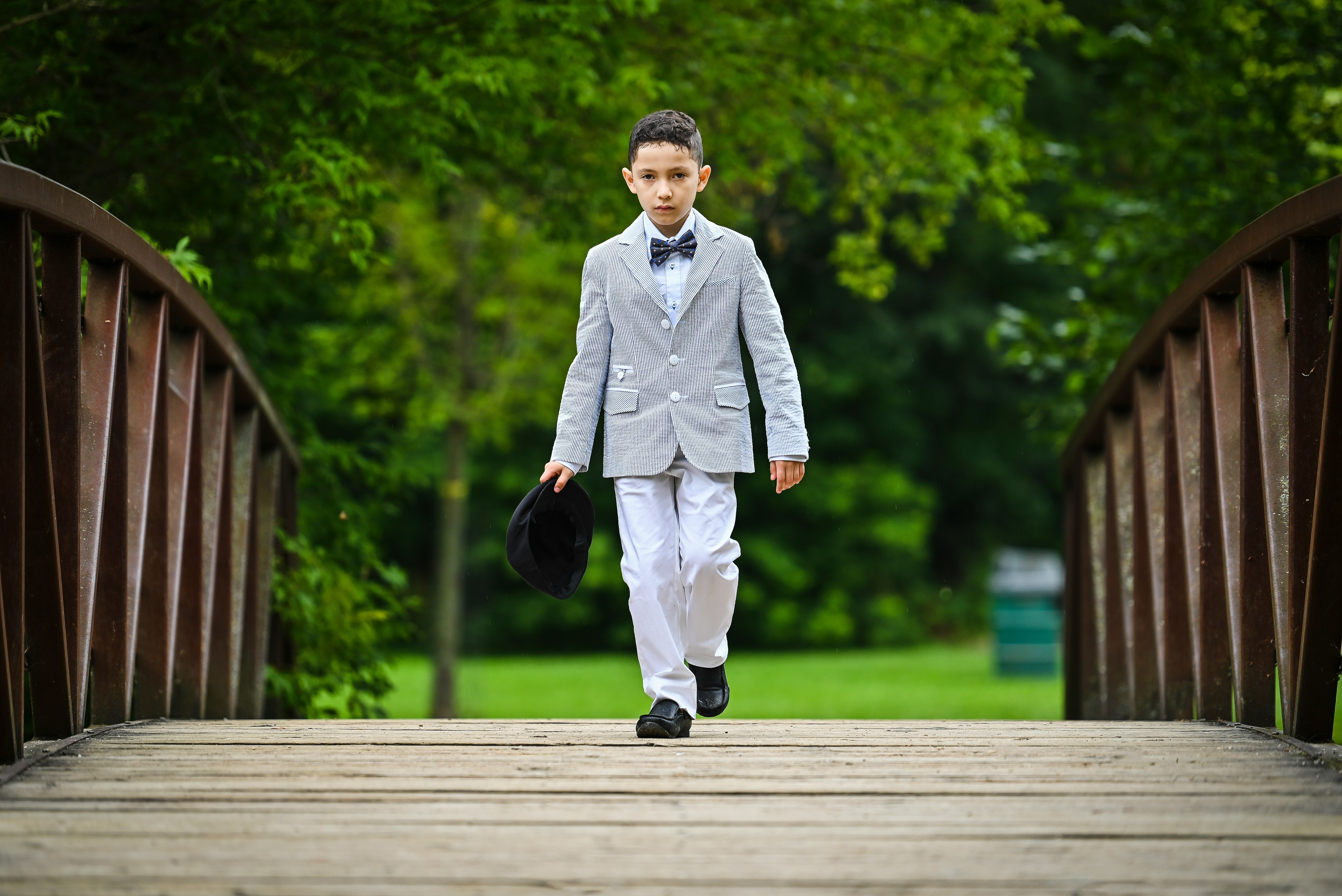 man in white suit and black pants standing on wooden bridge