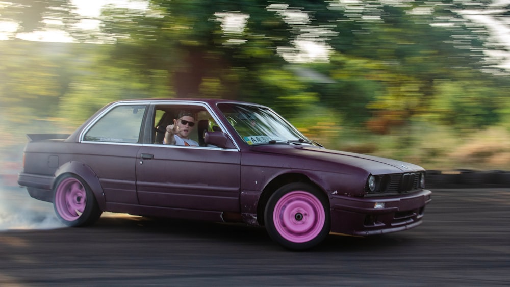 man in black shirt driving purple sedan on road during daytime