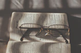 Close-up of an open Bible with glasses resting on the page, sunlight shining through