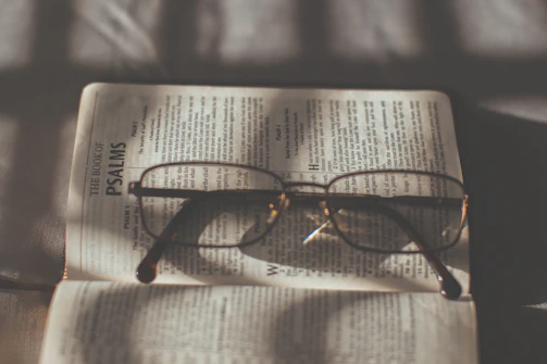 Close-up of an open Bible with glasses resting on the page, sunlight shining through