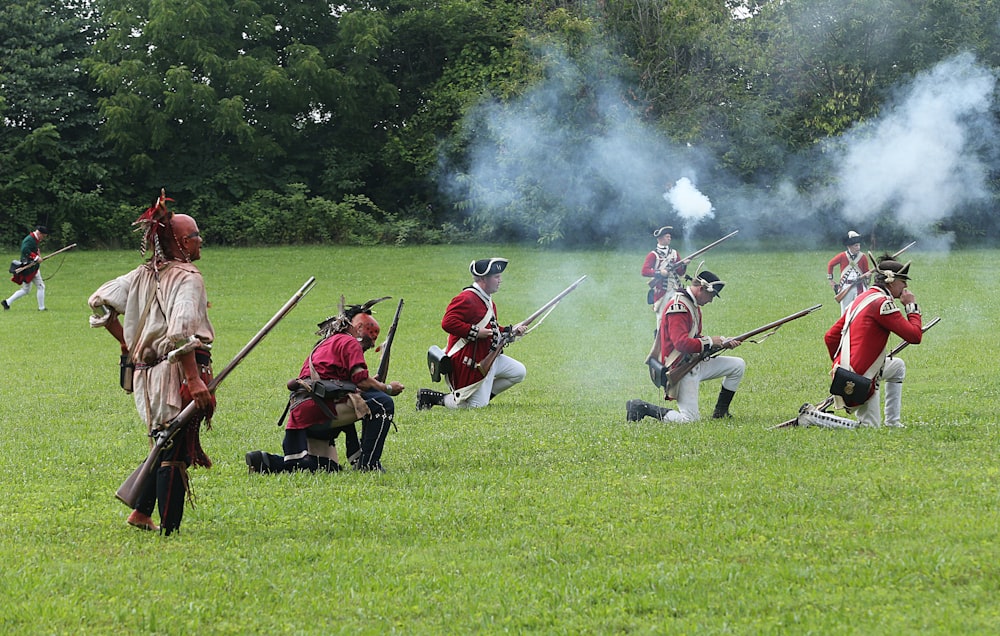 people in red and black robe holding rifle on green grass field during daytime