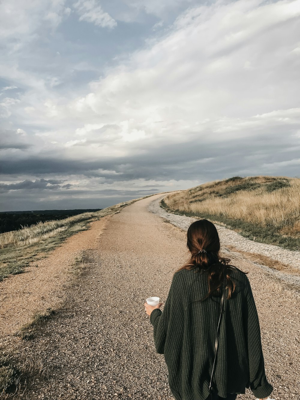 woman in black coat standing on brown dirt road during daytime