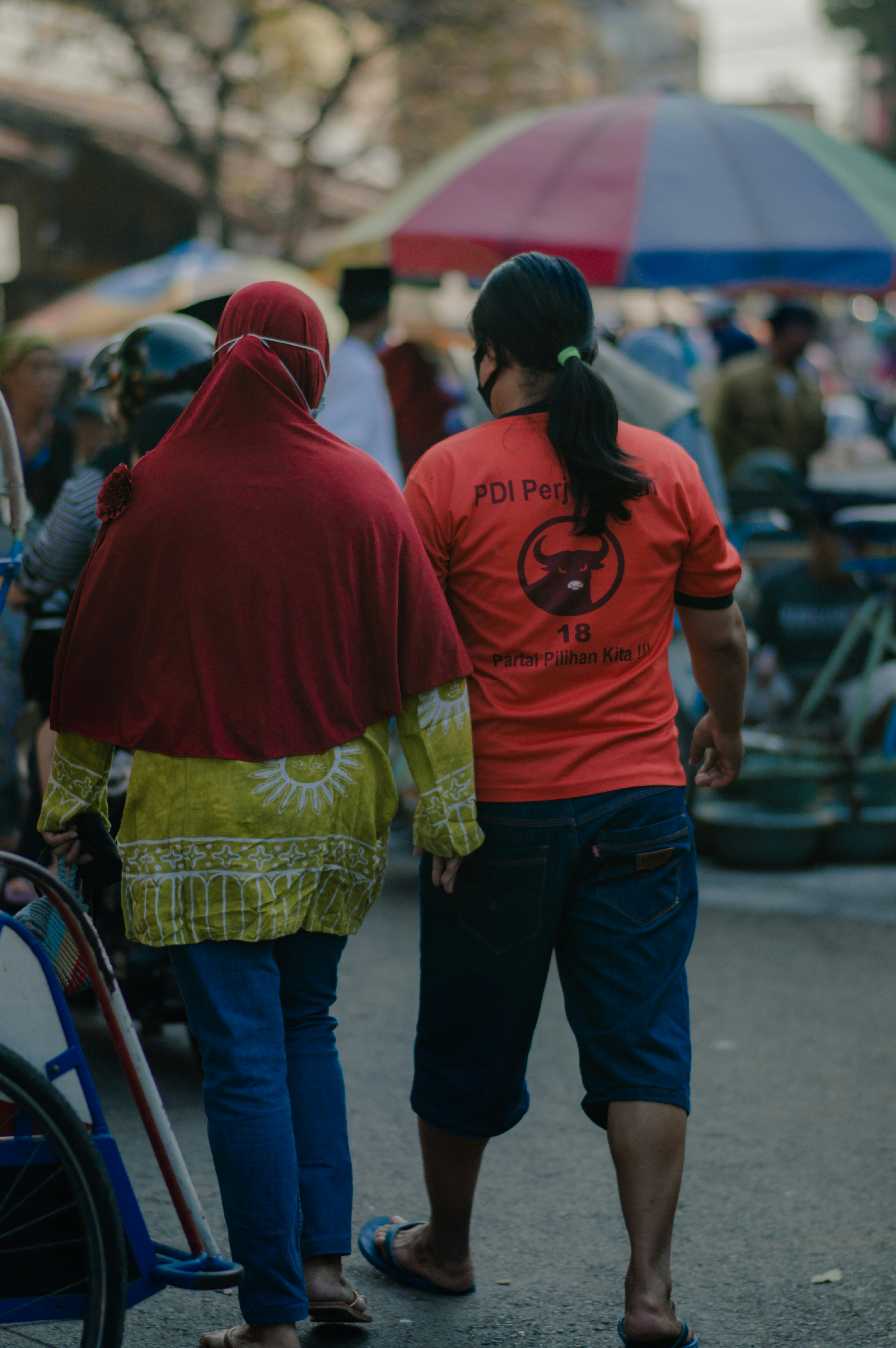 Pria berhoodie merah berdiri di samping wanita berjaket kuning
