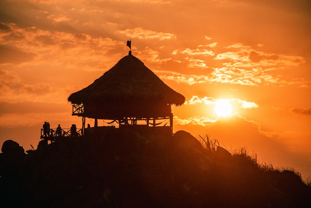 silhouette of people standing near brown wooden gazebo during sunset