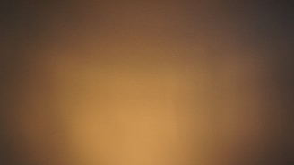 A smooth wall surface bathed in warm, subdued lighting, creating a gradient effect from darker brown tones on the edges to lighter beige in the center.