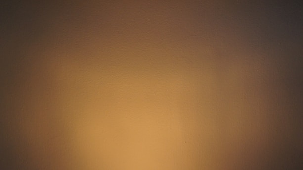 A smooth wall surface bathed in warm, subdued lighting, creating a gradient effect from darker brown tones on the edges to lighter beige in the center.
