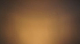 A smooth wall surface bathed in warm, subdued lighting, creating a gradient effect from darker brown tones on the edges to lighter beige in the center.