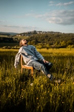 man in gray hoodie sitting on brown wooden chair on green grass field during daytime
