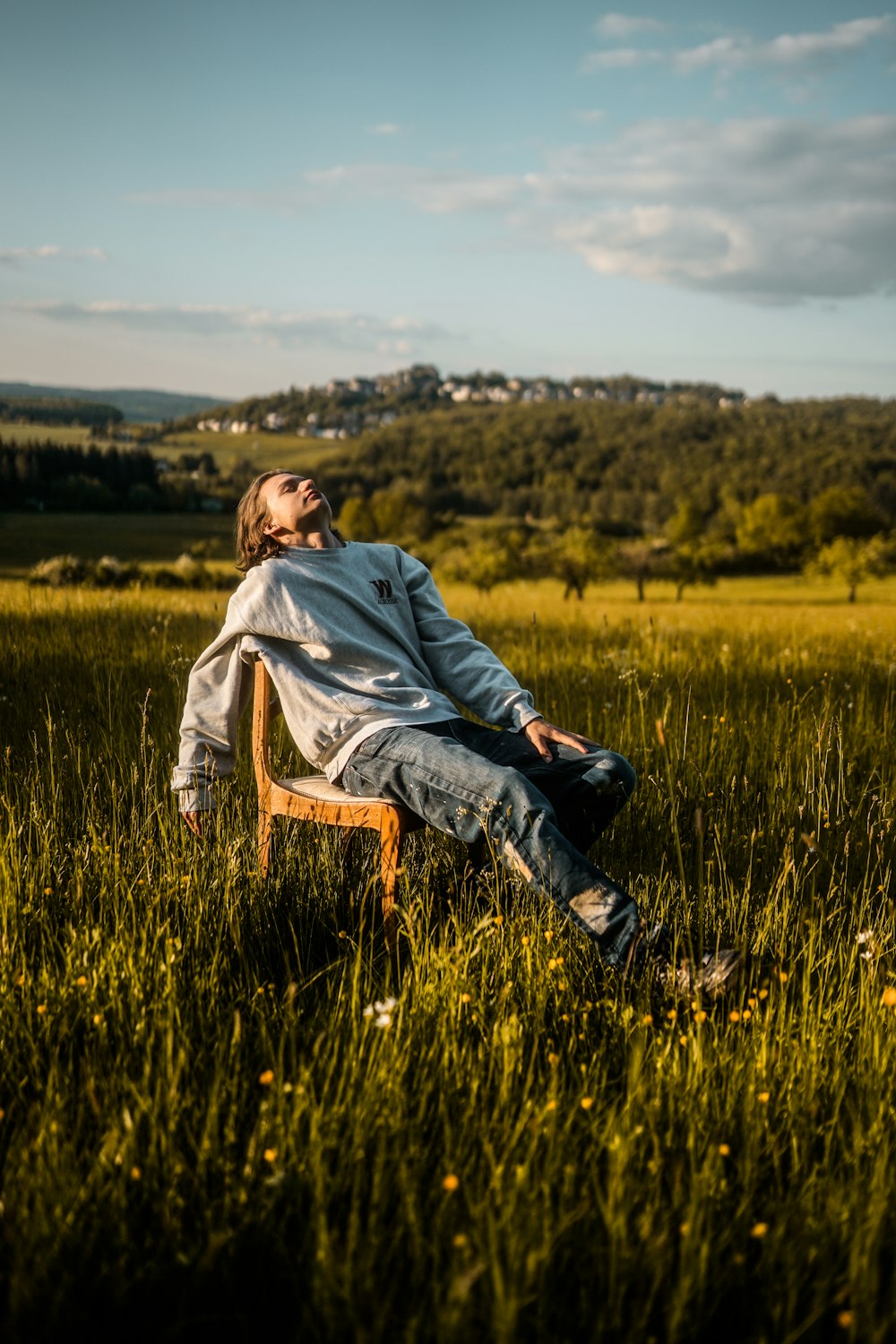 회색 후드티를 입은 남자가 낮에 푸른 잔디밭에 갈색 나무 의자에 앉아 있습니다.