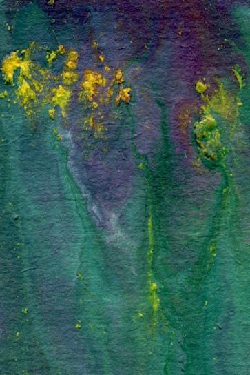 An abstract watercolor painting features a blend of deep green, purple, and scattered bursts of bright yellow. The textured background creates a fluid and organic appearance, with colors merging seamlessly.
