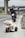 A small toy motorcycle is placed on the roadside of a highway. Behind the toy motorcycle, there is a larger real motorcycle parked on the side of the road. The road is deserted with no other vehicles in sight, and there are overpasses in the background.