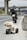 A small toy motorcycle is placed on the roadside of a highway. Behind the toy motorcycle, there is a larger real motorcycle parked on the side of the road. The road is deserted with no other vehicles in sight, and there are overpasses in the background.