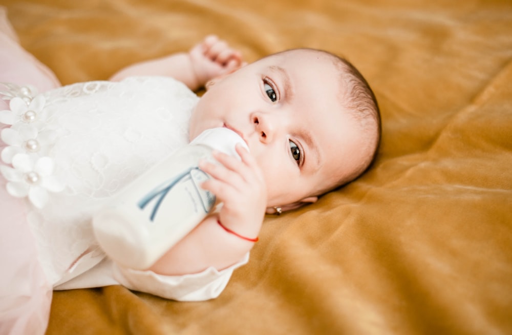 bébé en robe blanche couché sur textile jaune