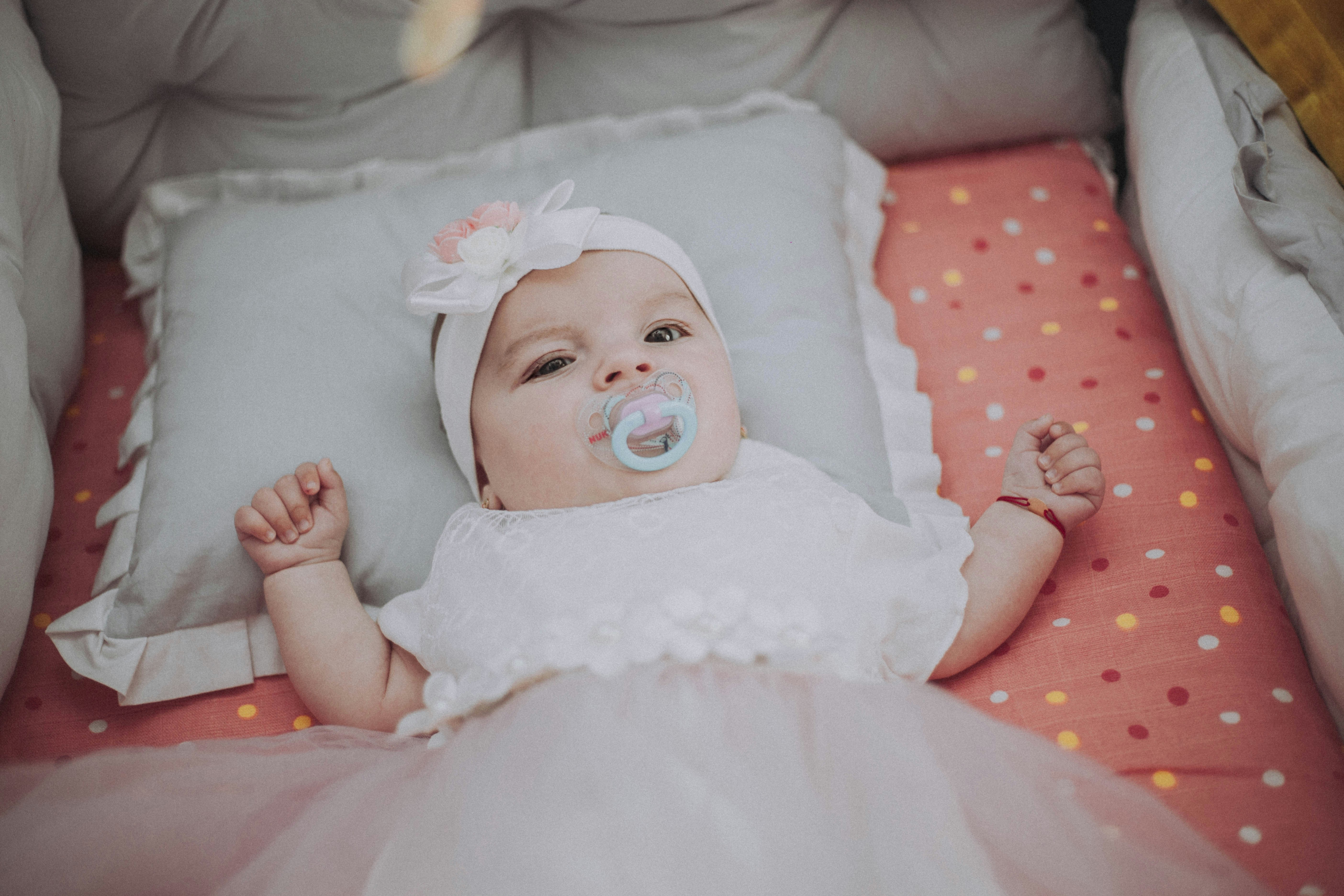 baby in white dress lying on bed