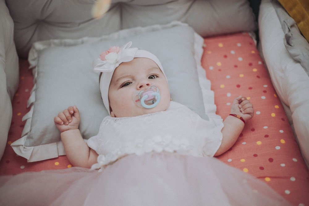 baby in white dress lying on bed