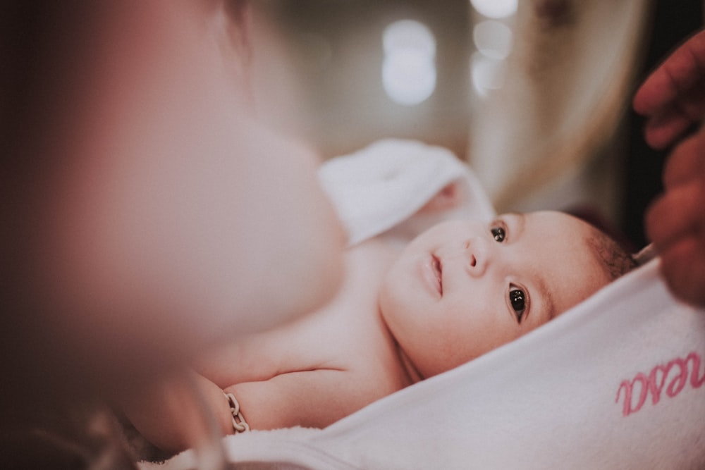 baby lying on white textile