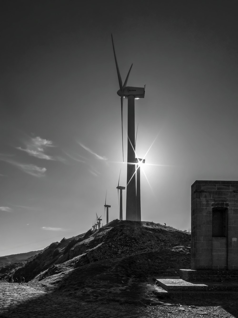 grayscale photo of wind mill on rocky hill