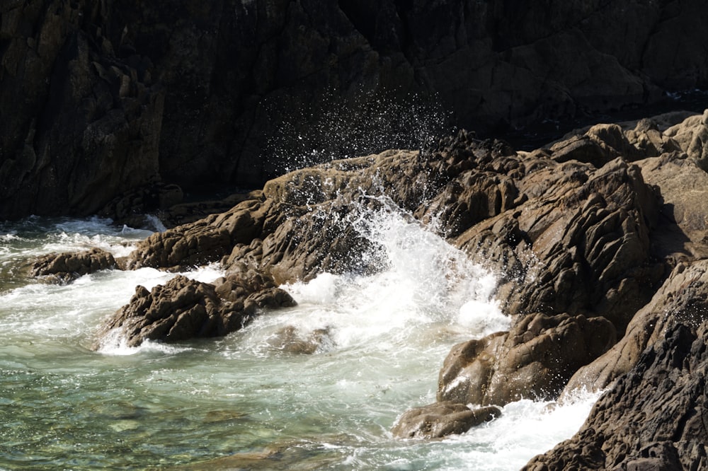 ondas de água atingindo a formação rochosa marrom durante o dia