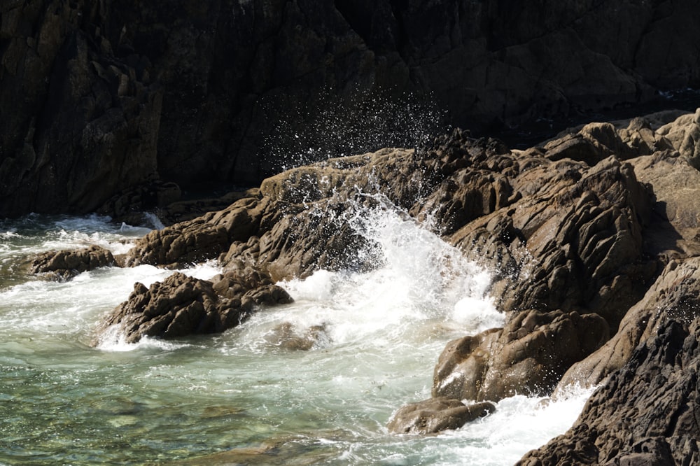 water waves hitting brown rock formation during daytime