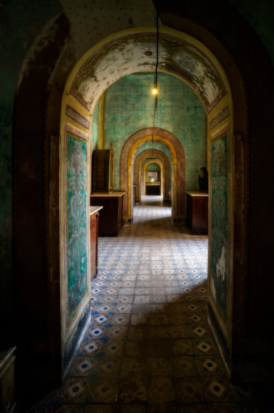 Long, narrow hallway with green and white tiled floor, ornate decorations, and large archway