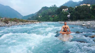 A traveler meditating near a sacred river, surrounded by lush greenery.