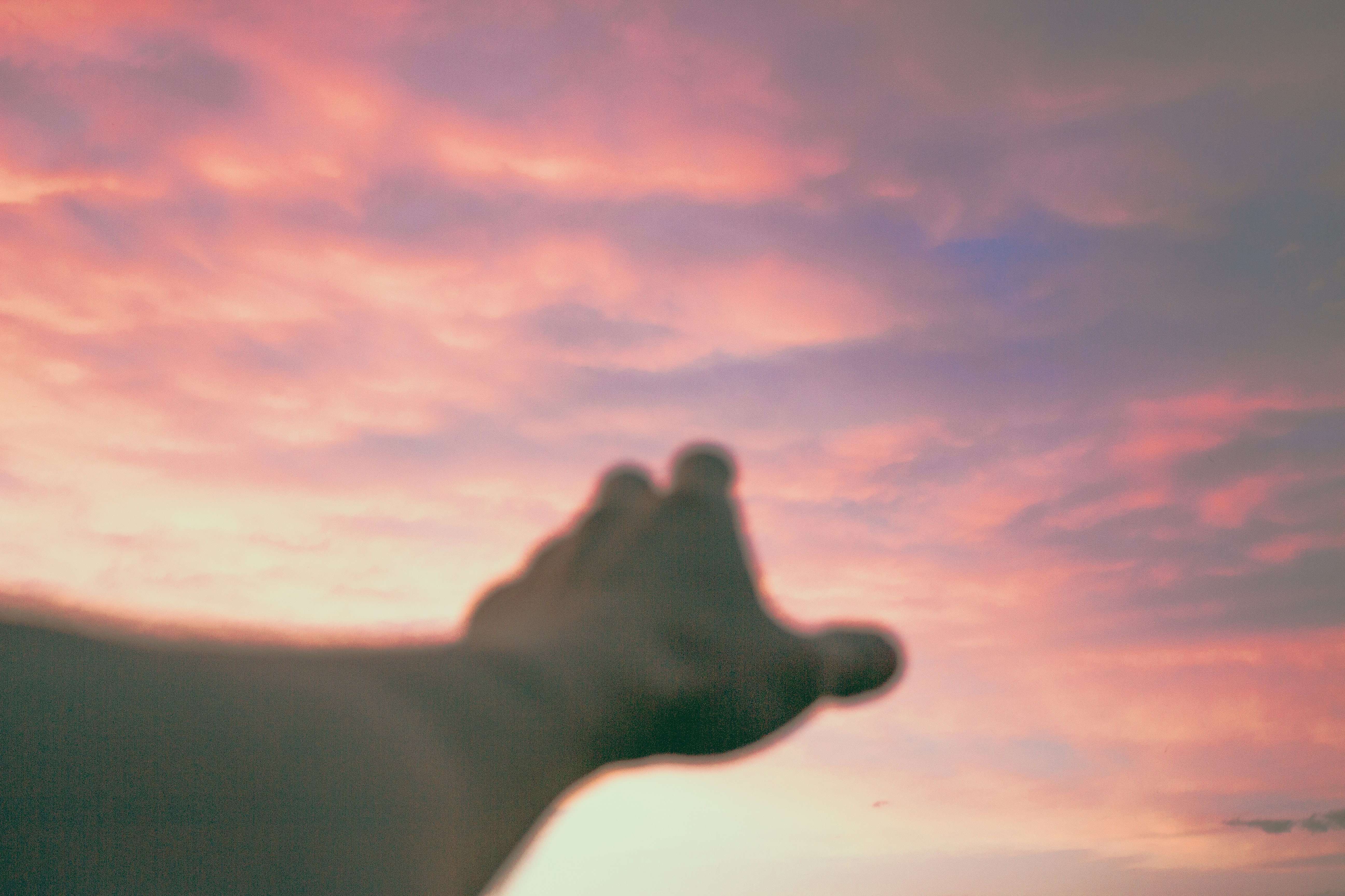 silhouette of persons right hand under cloudy sky during sunset