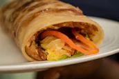 Freshly wrapped shawarma roll with juicy chicken and colorful veggies peeking out.