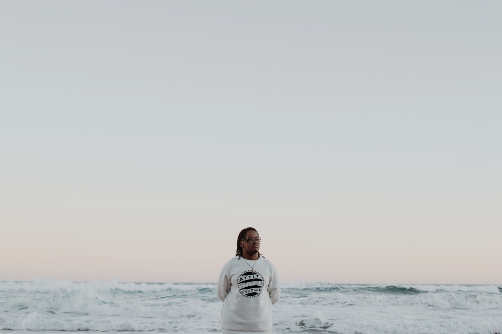 man in white crew neck t-shirt standing on sea shore during daytime