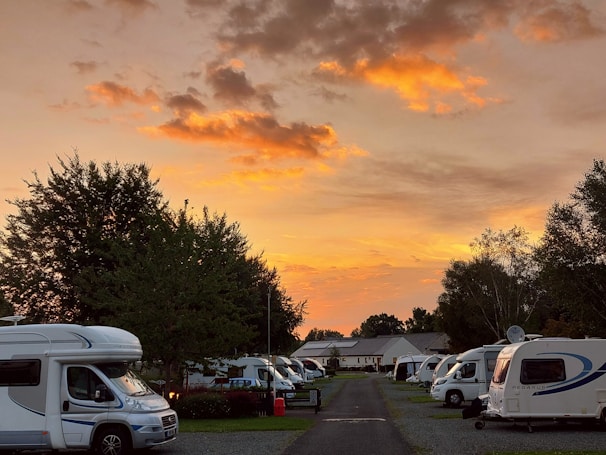 Sunset casting warm orange hues over a serene campsite with tents and camper vans.