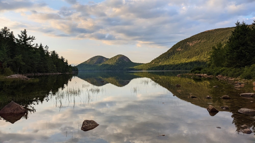 Montagne verte à côté d’un plan d’eau sous un ciel nuageux pendant la journée