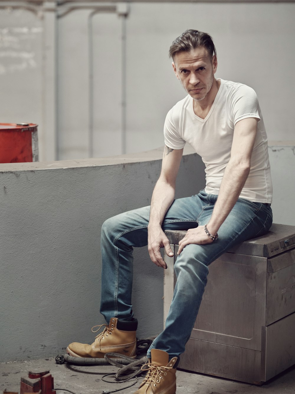 man in white crew neck t-shirt and blue denim jeans sitting on gray concrete bench