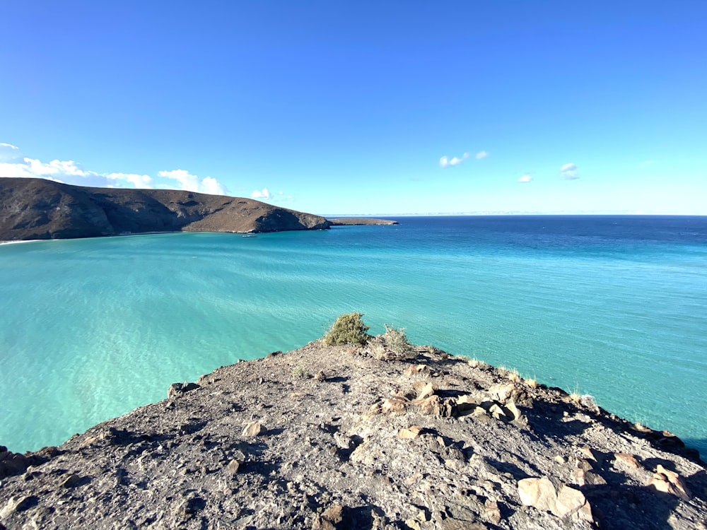 blaues Meer neben braunem Rocky Mountain unter blauem Himmel tagsüber