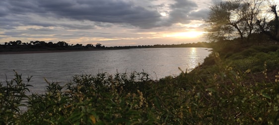 A tranquil riverside scene in Thailand at sunset, with soft golden light reflecting on calm waters and lush greenery.