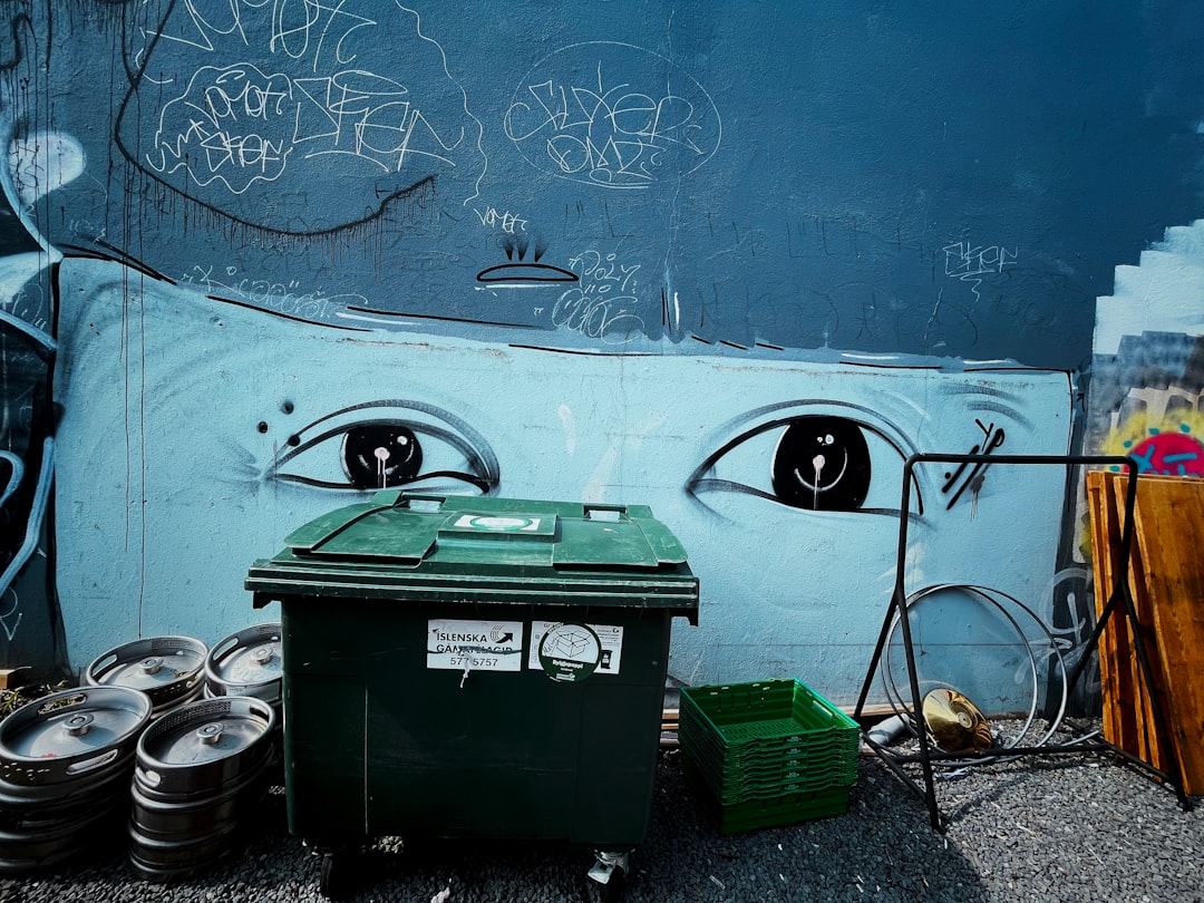 black and green trash bin beside blue wall