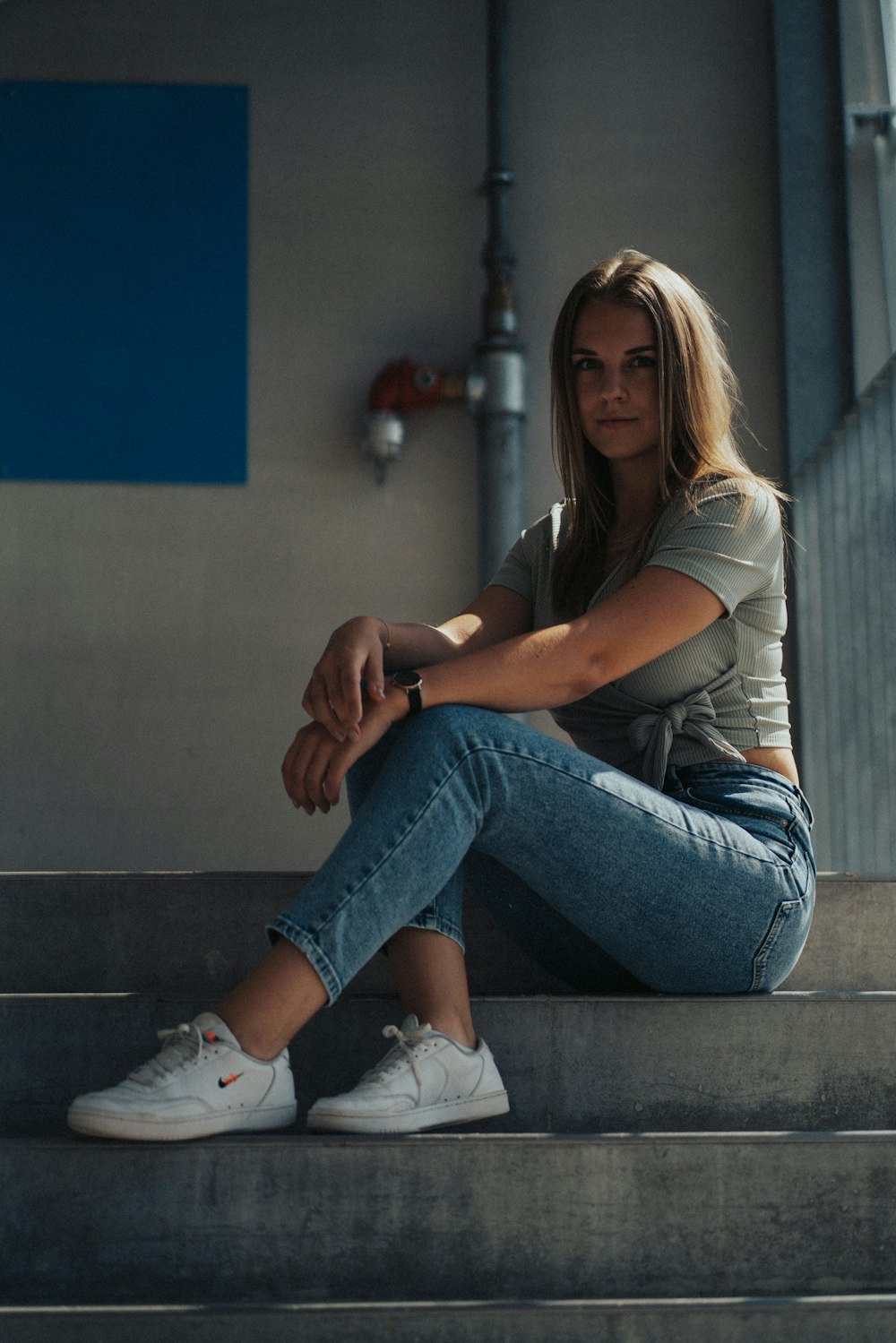 woman in gray t-shirt and blue denim jeans sitting on gray concrete stairs