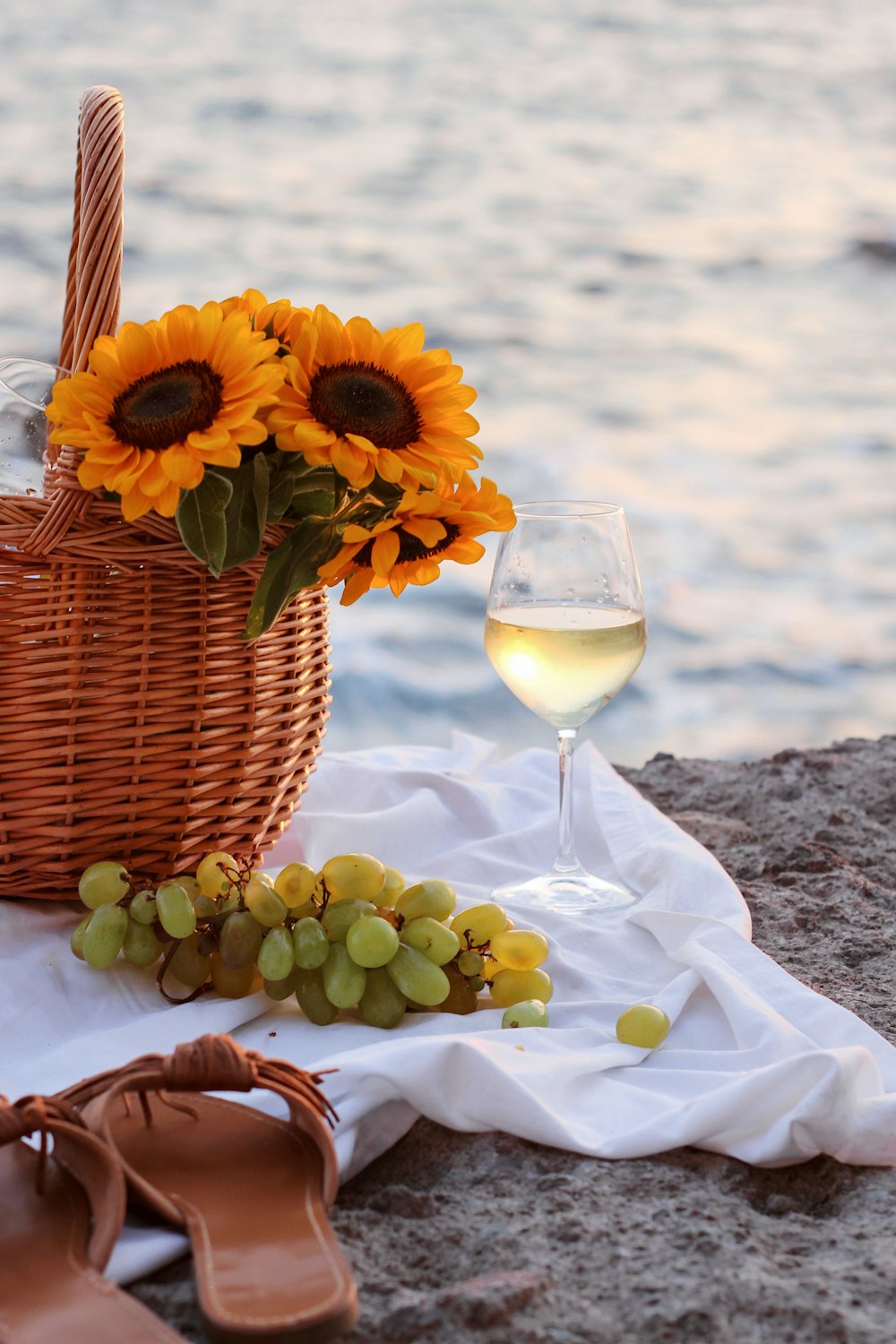 girasol amarillo en canasta tejida marrón junto a copa de vino transparente sobre tela blanca