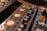 A close-up view of audio equipment featuring various control knobs and LED indicators. The foreground shows a VU meter with glowing orange backlighting, and to the side, there are connectors for audio cables, including an orange plug.
