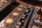A close-up view of audio equipment featuring various control knobs and LED indicators. The foreground shows a VU meter with glowing orange backlighting, and to the side, there are connectors for audio cables, including an orange plug.