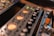A close-up view of audio equipment featuring various control knobs and LED indicators. The foreground shows a VU meter with glowing orange backlighting, and to the side, there are connectors for audio cables, including an orange plug.