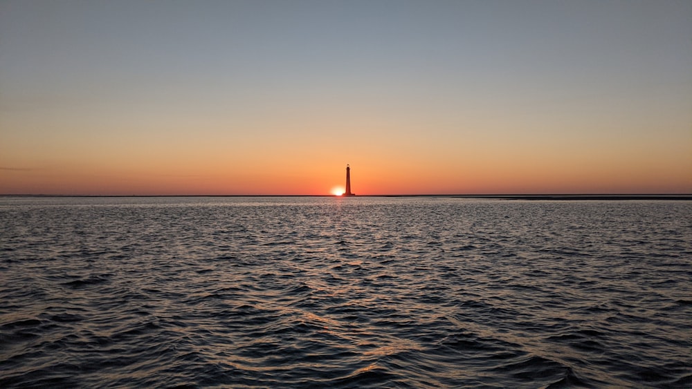 silhouette of lighthouse on sea during sunset