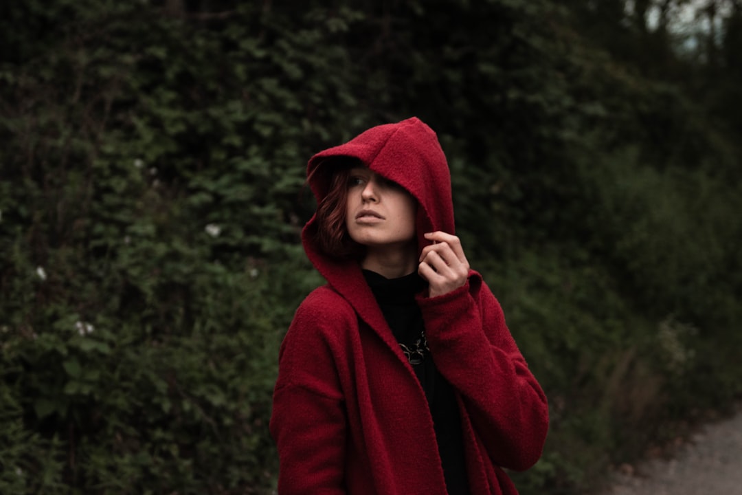 woman in red hoodie standing near green trees during daytime