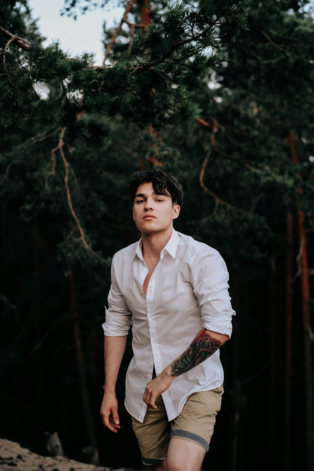 man in white dress shirt standing near green trees during daytime