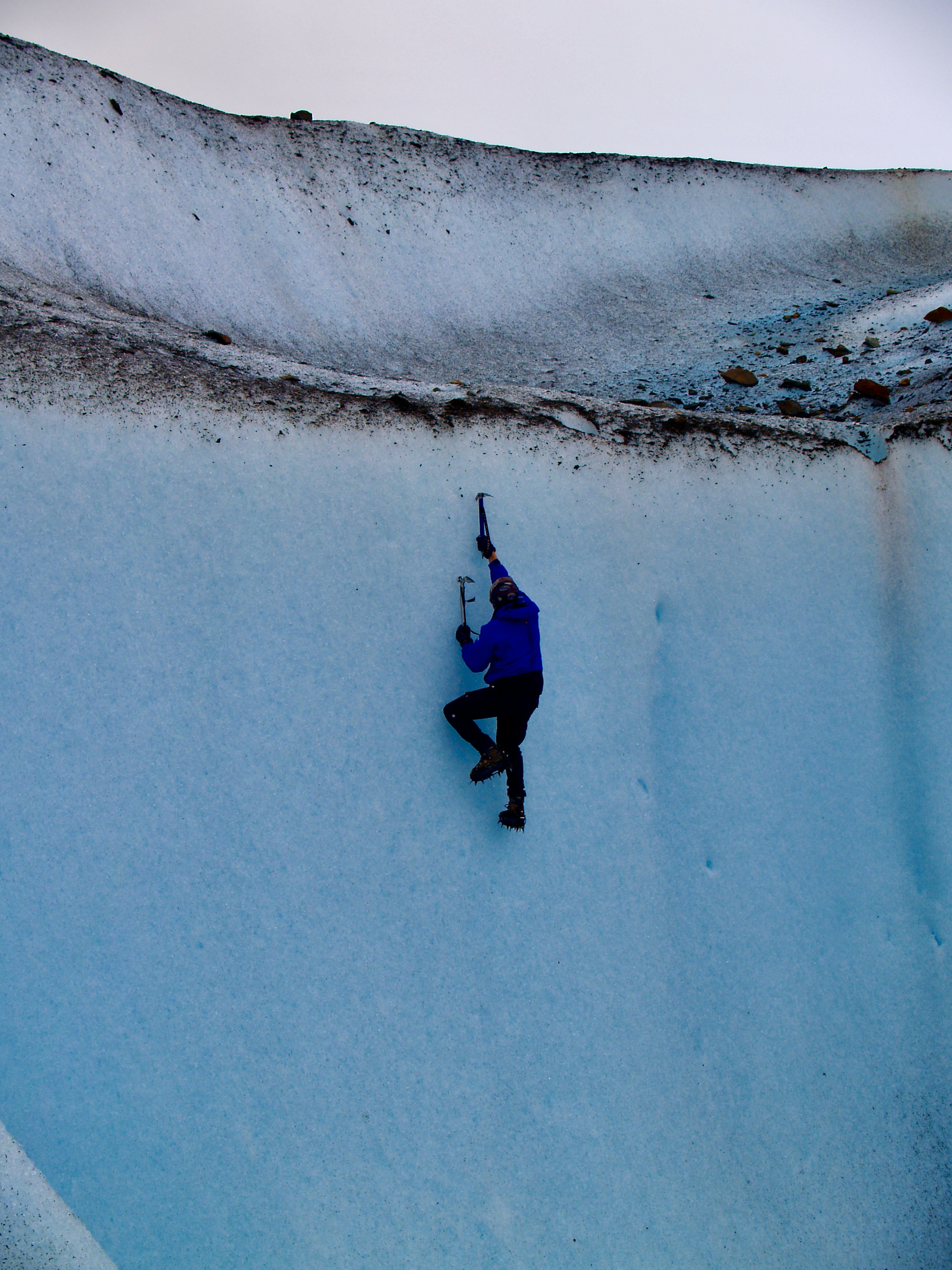 Ice climber on blue glacier wall in Iceland with crevasses and ice formations in background